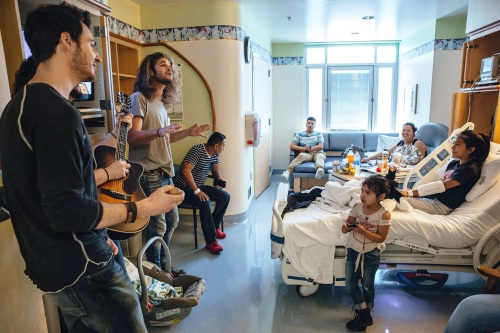 The band Levon plays for a family at a younger patient's bedside. The little sister of the patient shyly looks up at the band and smiles